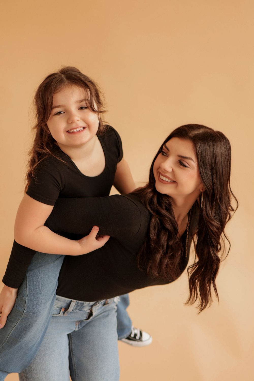 Two people in casual attire share joyful moments against neutral background.