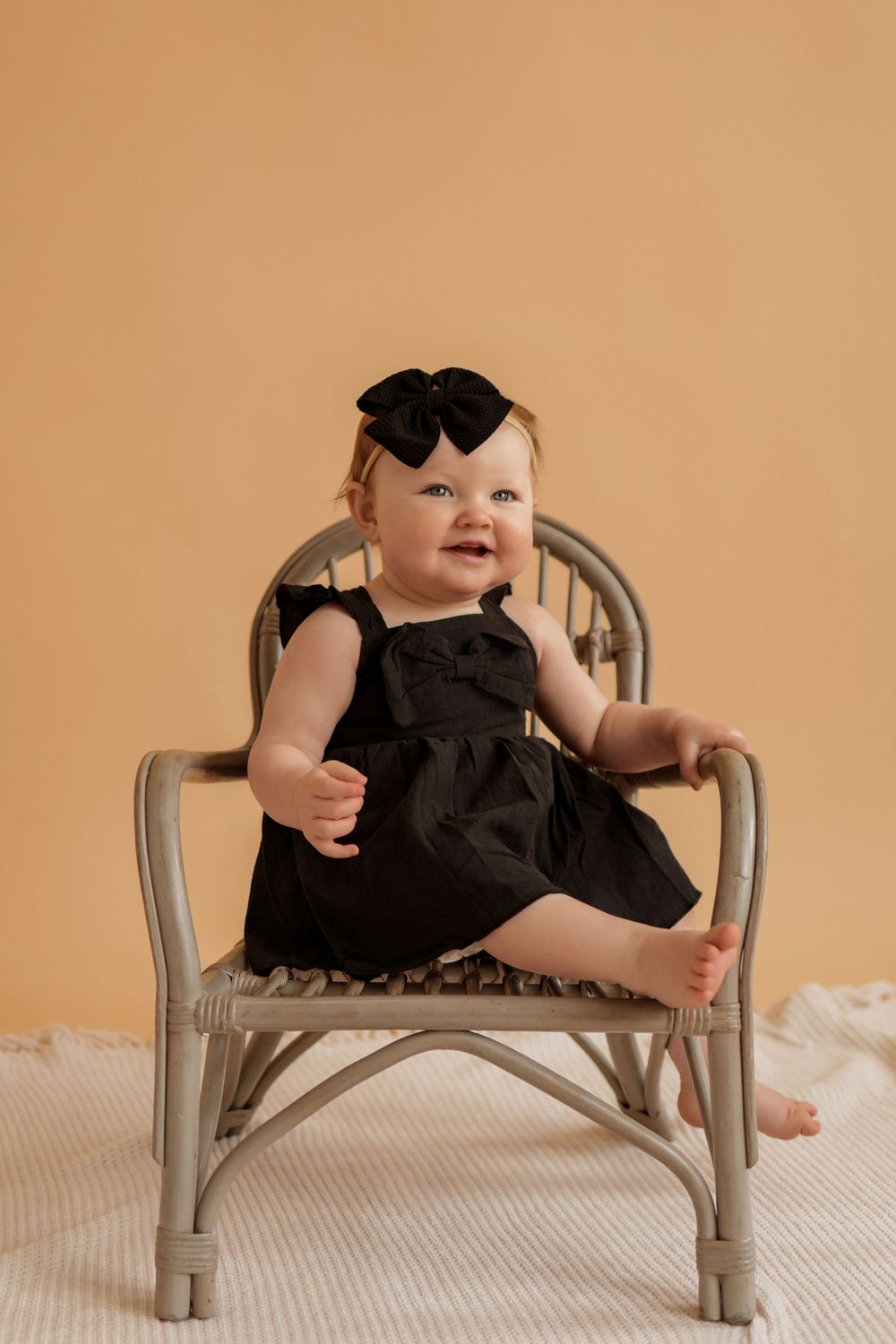 Infant wearing black outfit stretches and plays on miniature gray bench.