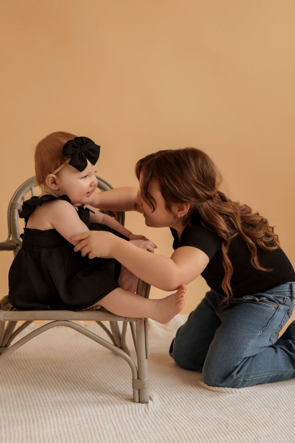 Mother and baby share tender moment on gray chair during photo session.