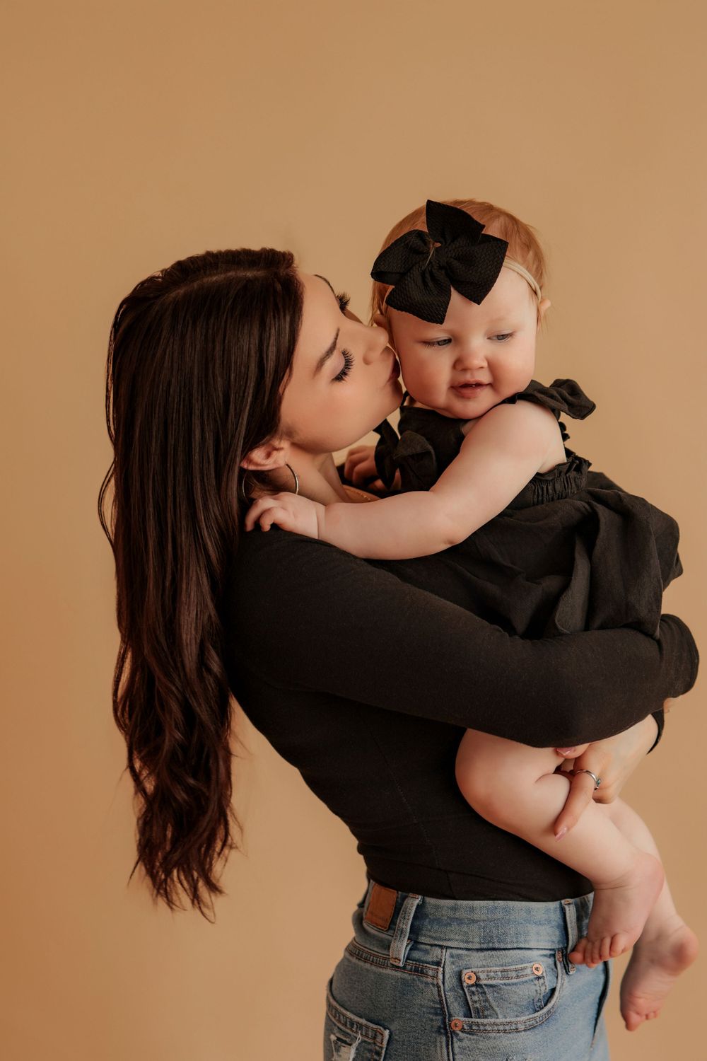 Mother holding baby in black outfit during studio photography session.