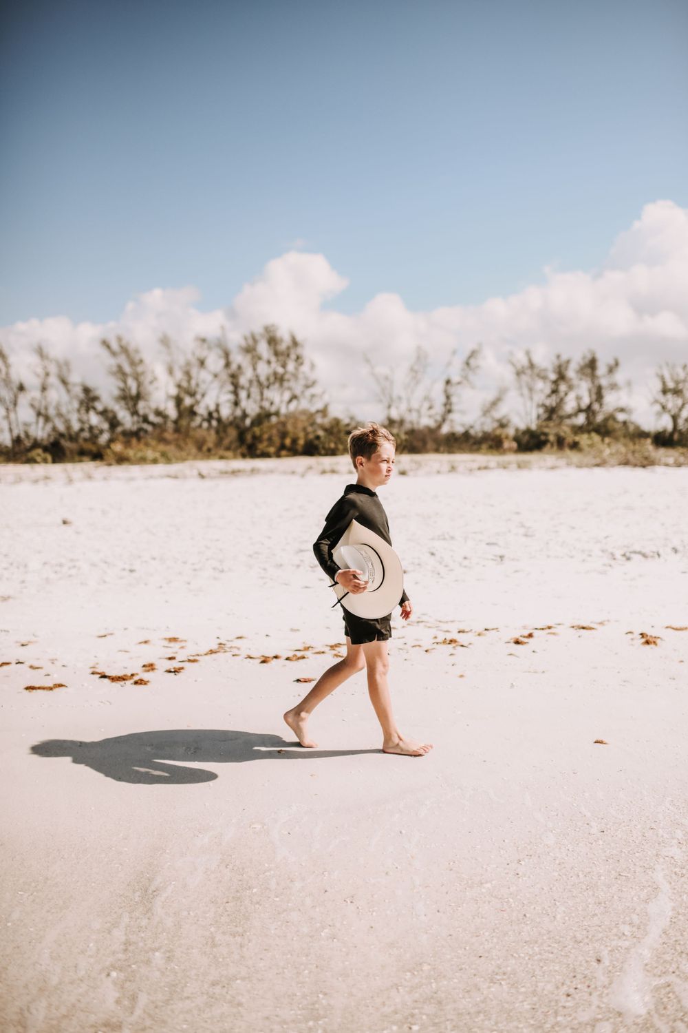 A sequence of photos showing a small child running and playing on a pristine white sandy beach  on lido key under a bright blue sky.