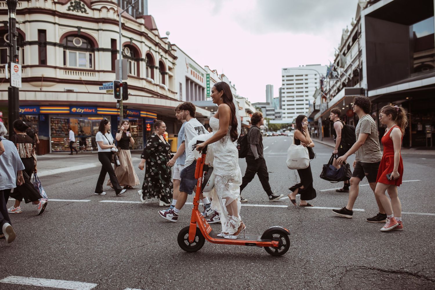 People navigate a busy urban intersection as someone rides an electric scooter through a crowded street corner.