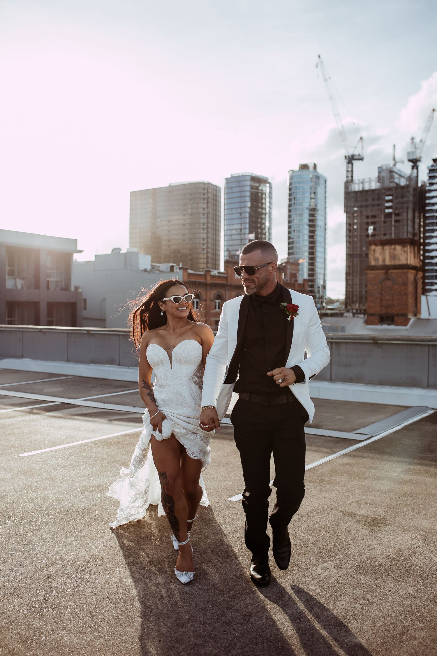 A couple celebrates on an urban rooftop parking lot with high-rise buildings and construction cranes in the background.