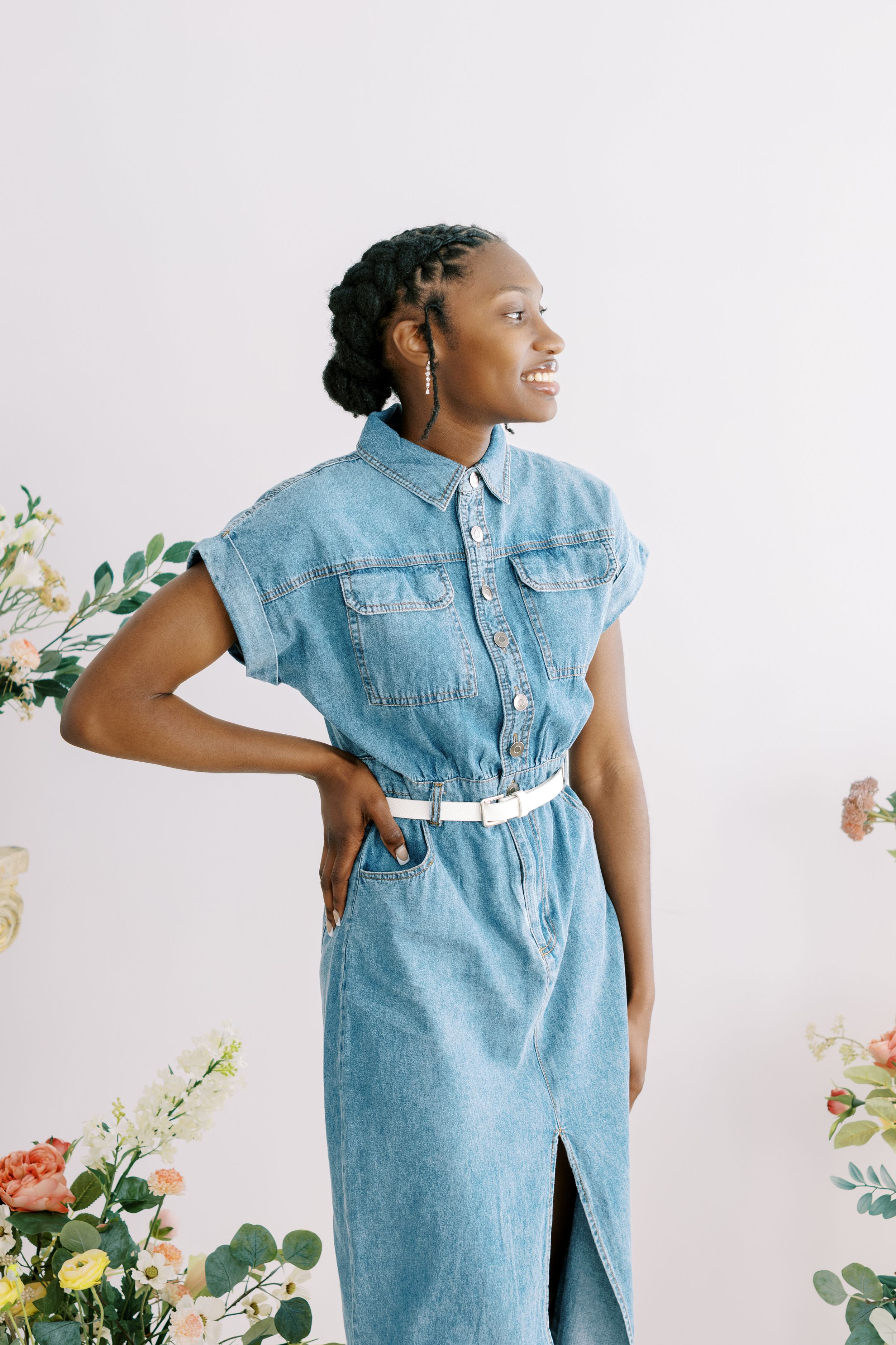 A model poses in a light blue denim dress with ruffled sleeves against a floral backdrop.