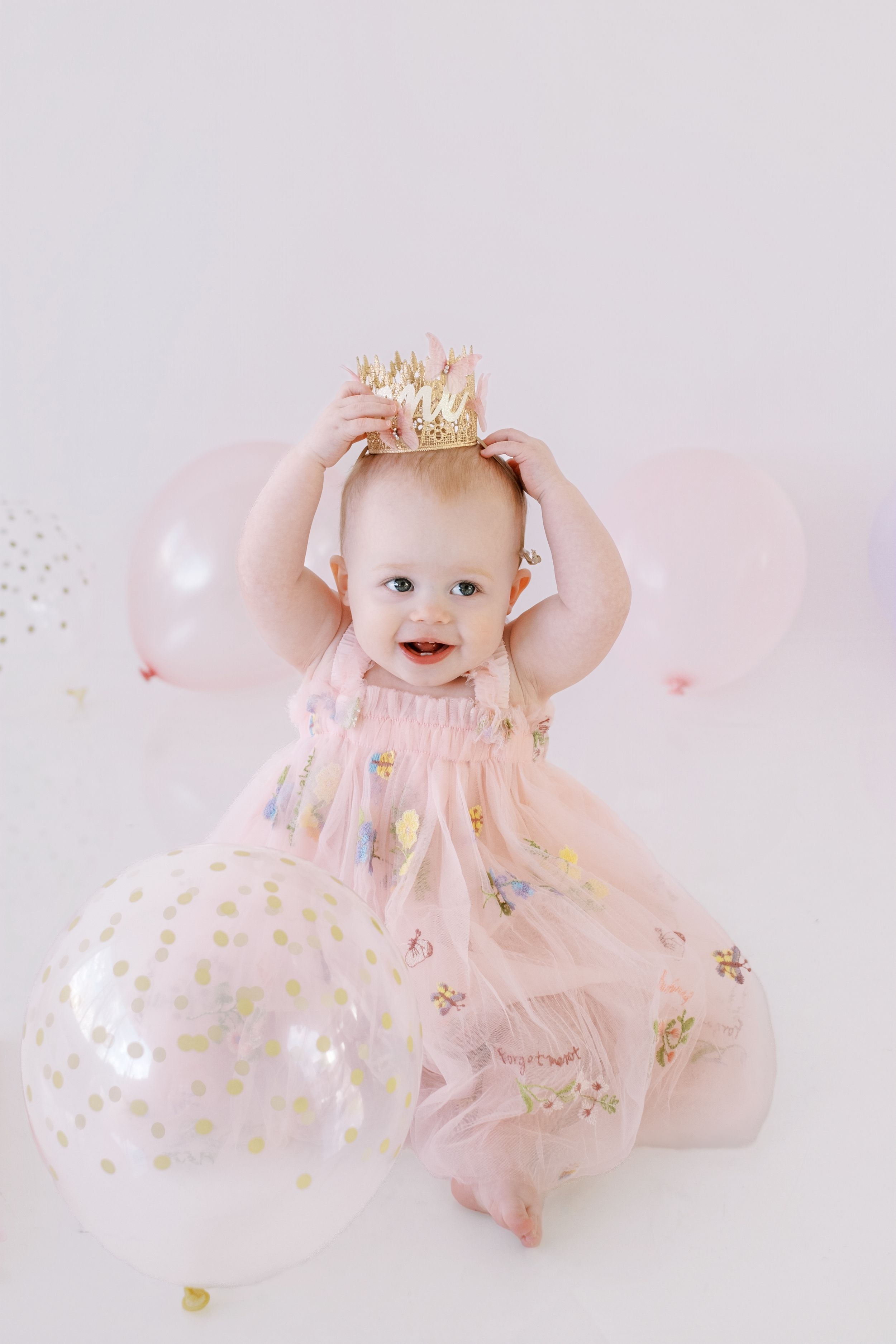 Baby wearing pink tulle dress and gold crown poses on pink background in sweet milestone photo session series.