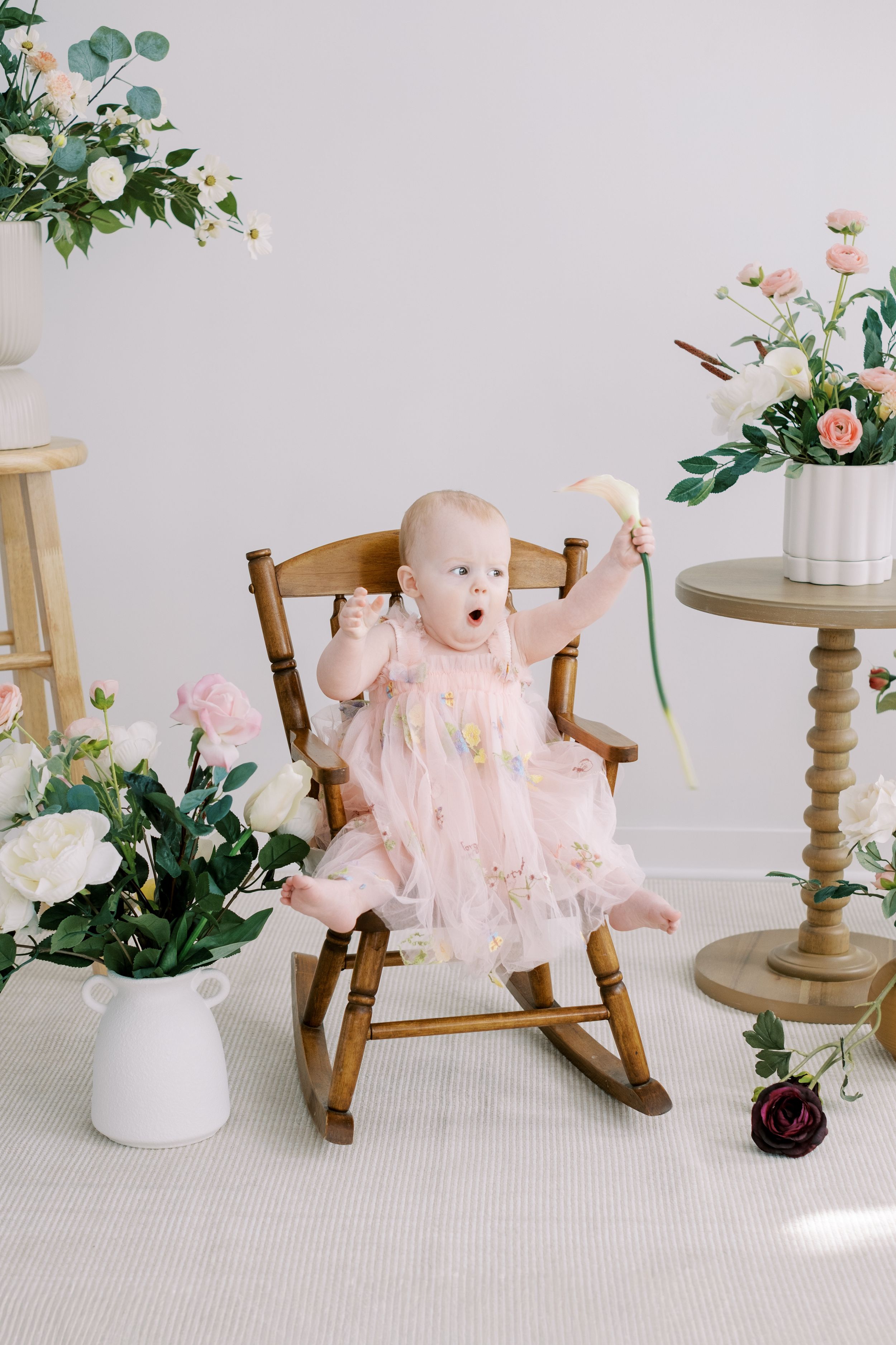 Pink plush bunny toy in rocking chair with floral decor and cake stand creating a whimsical nursery scene.