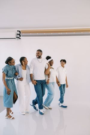 Family wearing coordinated white and denim outfits walks together against white background in casual photoshoot.