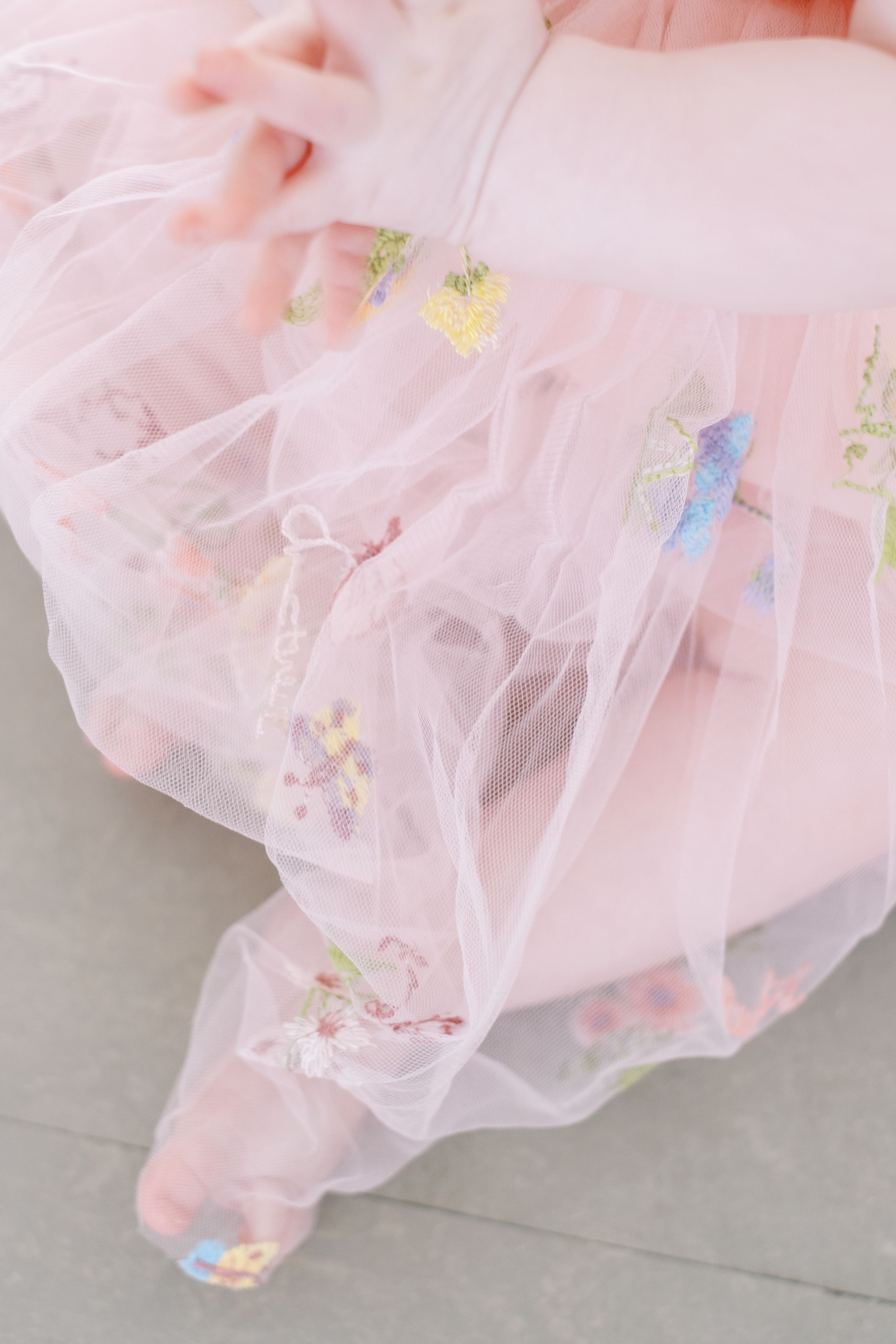 Delicate pink tulle fabric with embroidered floral details and pastel accents creates a dreamy, romantic texture.