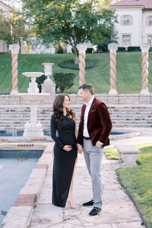 A couple shares a playful moment on stone steps in a garden setting with decorative columns and greenery.