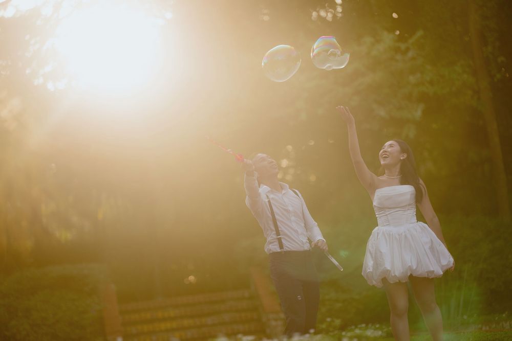 A couple in wedding attire walks through a sunlit garden path during golden hour.