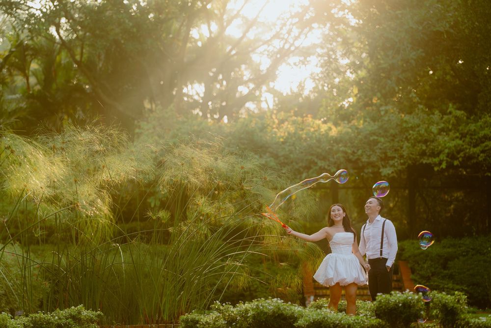 A couple poses together in a romantic garden setting during golden hour with sunlight filtering through trees.