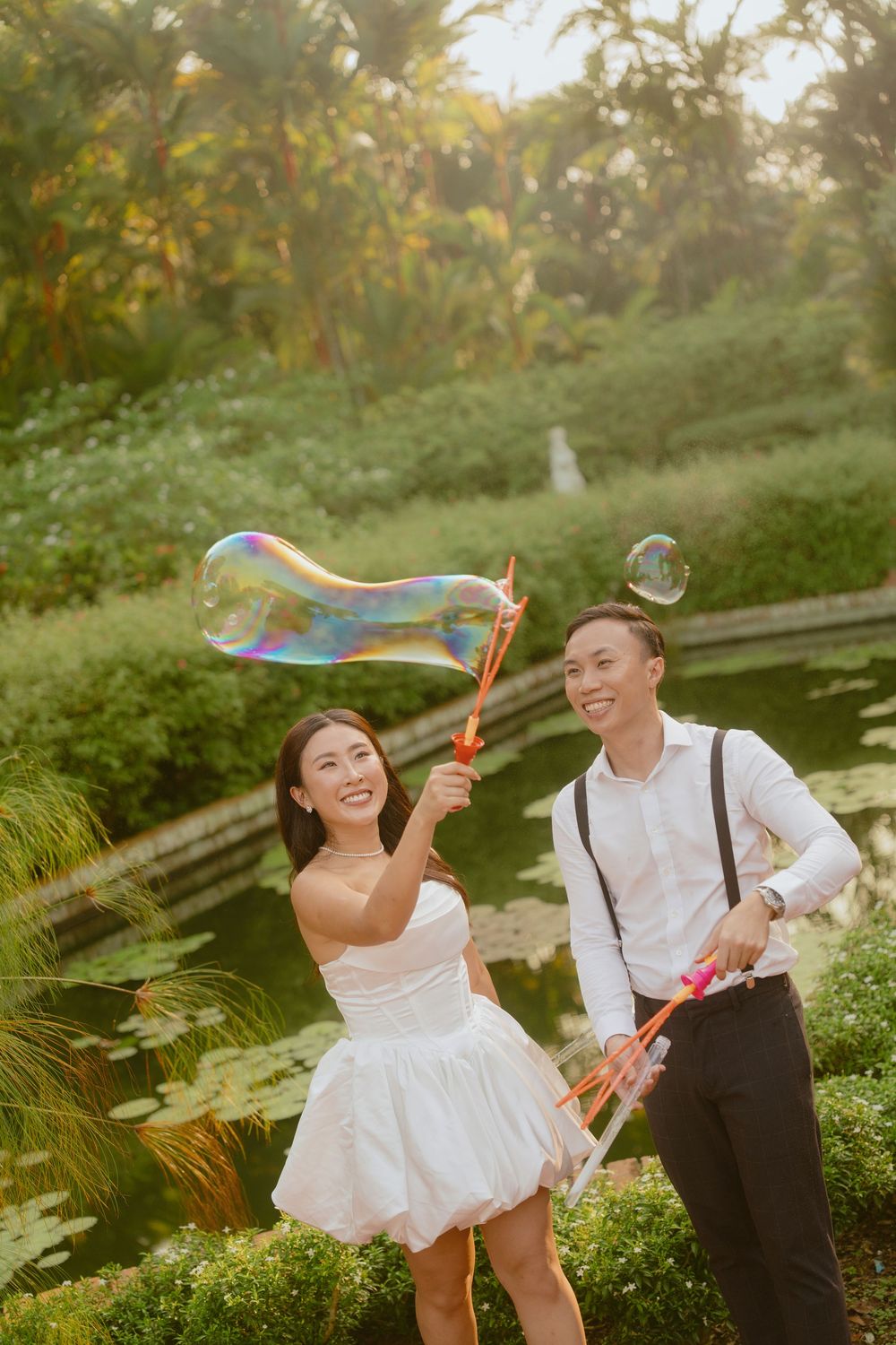 A couple plays with bubbles in a garden setting during their wedding photoshoot at sunset.