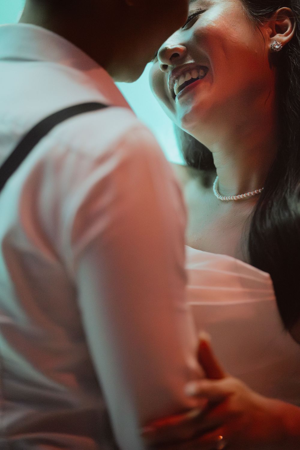 Intimate close-up shot of a joyful moment between couple bathed in dreamy blue and pink lighting.