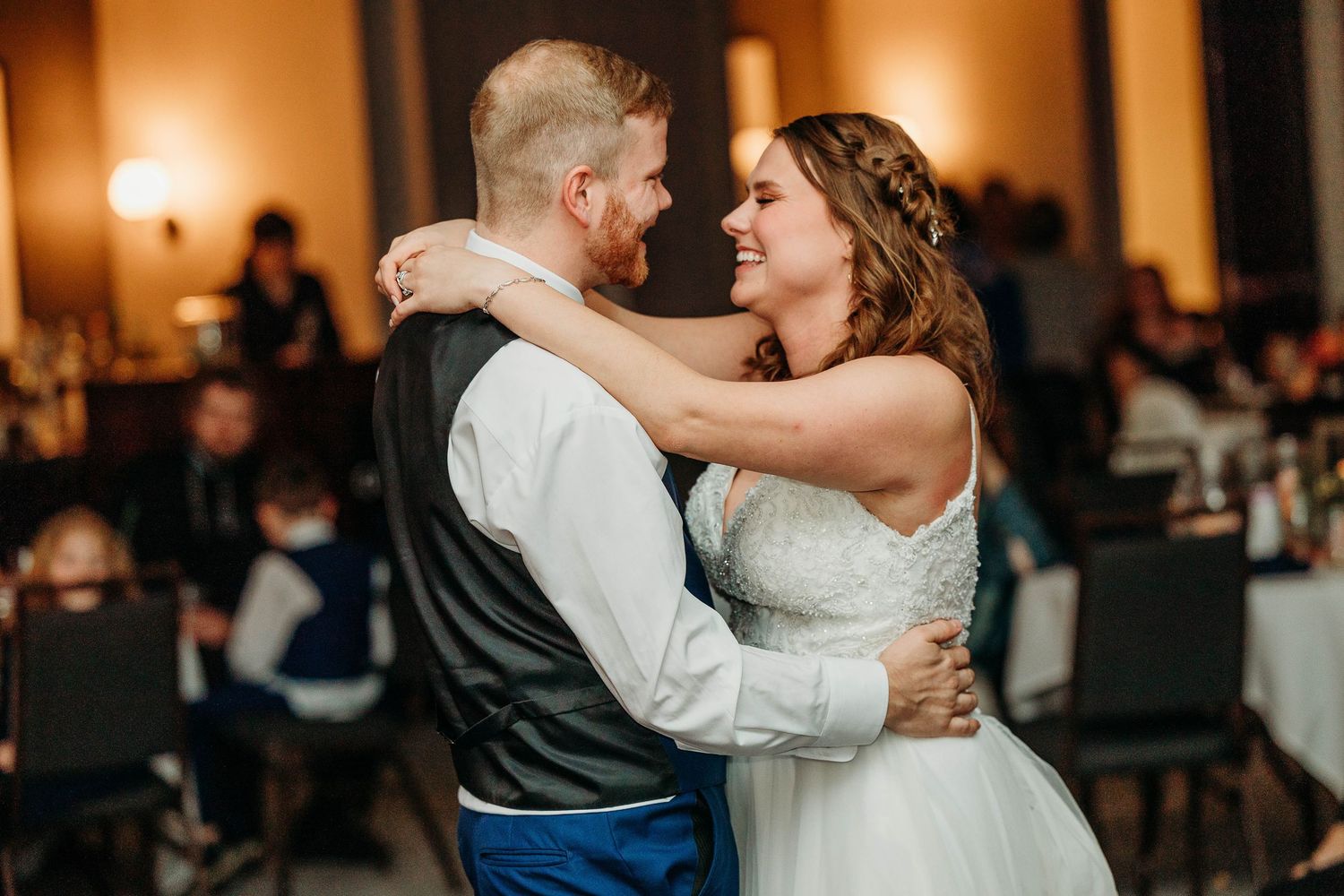 A couple shares an intimate dance together at an elegant wedding reception with warm lighting.