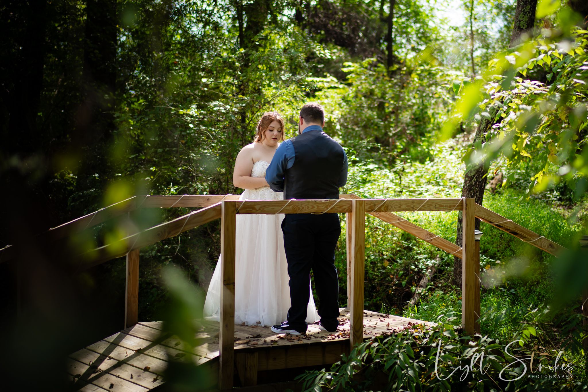 A couple shares an intimate moment exchanging vowels on a rustic wooden deck surrounded by lush green forest foliage.