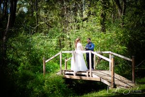 A couple shares an intimate moment exchanging vowels on a rustic wooden deck surrounded by lush green forest foliage.