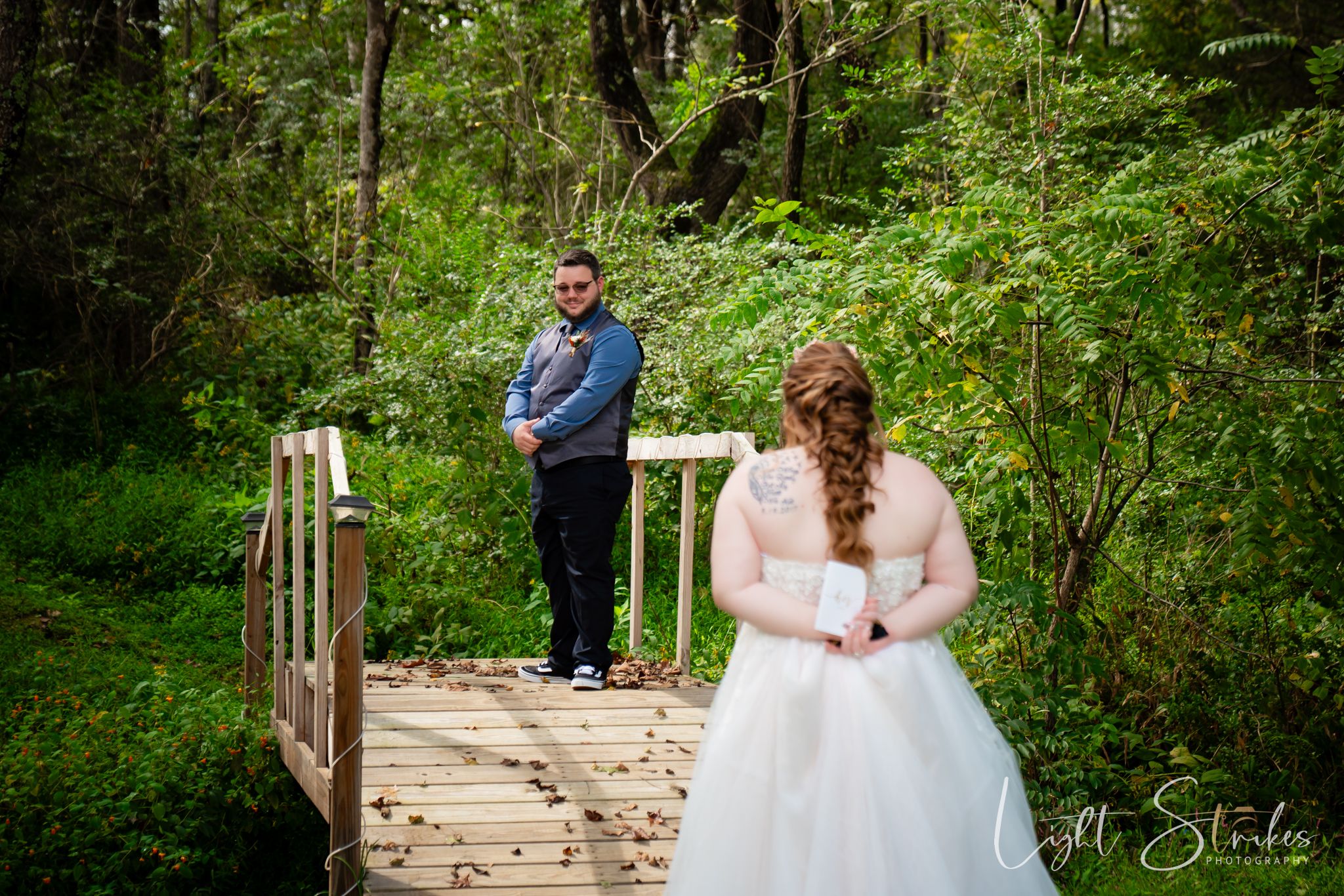 A first look between bride and groom on a rustic wooden bridge surrounded by lush green forest scenery.