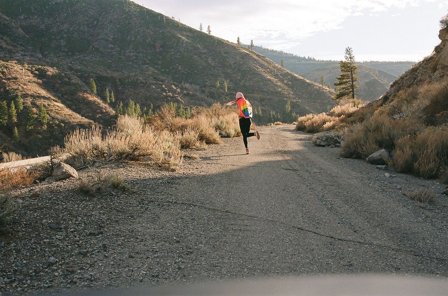 Person jogging on a winding mountain road during golden hour.