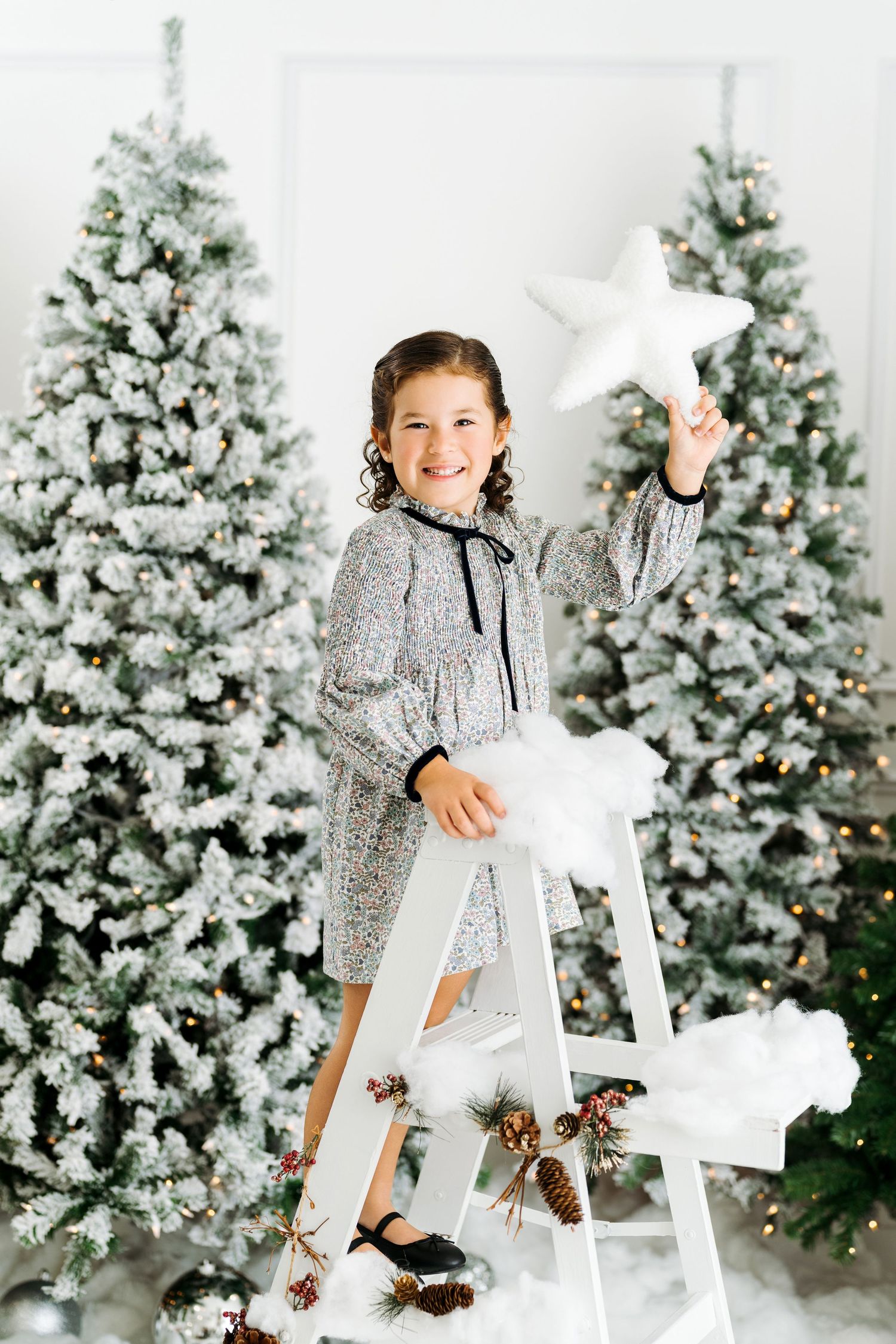 Little girl stand on white ladder and holding the star during Christmas photo session