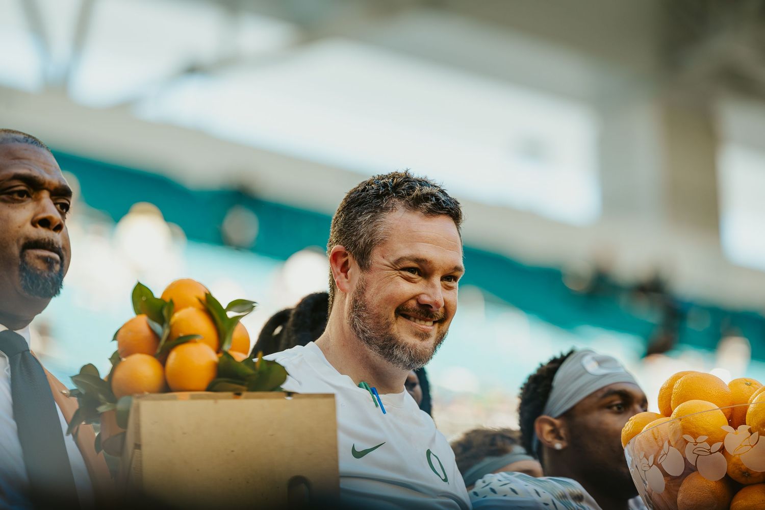 People at a farmers market smiling and laughing while looking at fresh oranges in boxes.