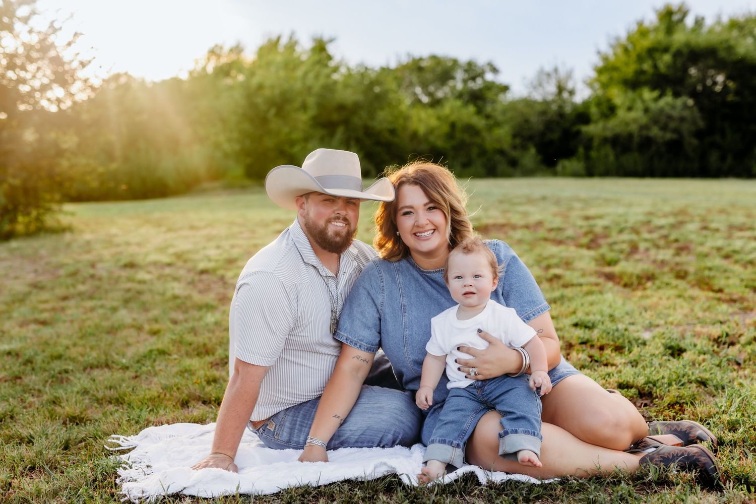 A family sits together in a grassy field during golden hour sunset, sharing tender moments and laughter.