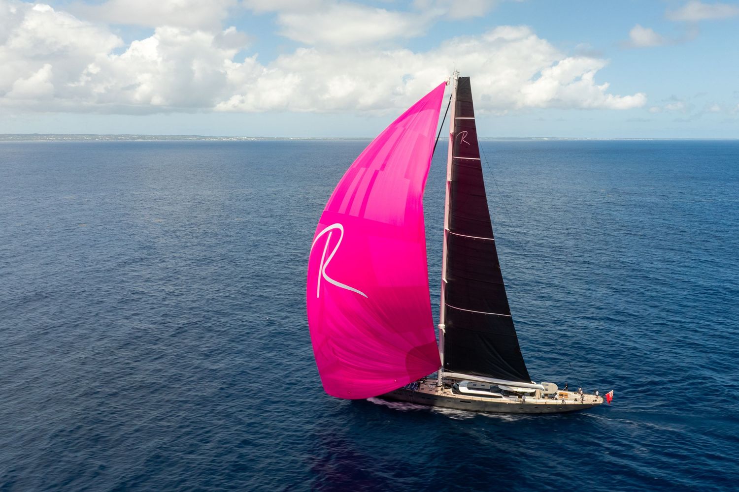 Sailing yacht with vibrant pink spinnaker sail deployed on open waters.