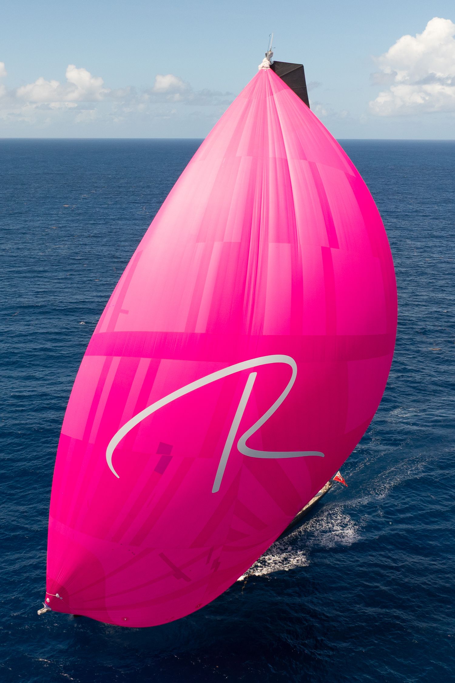 Luxury yacht flying bright pink spinnaker sail across deep blue ocean.