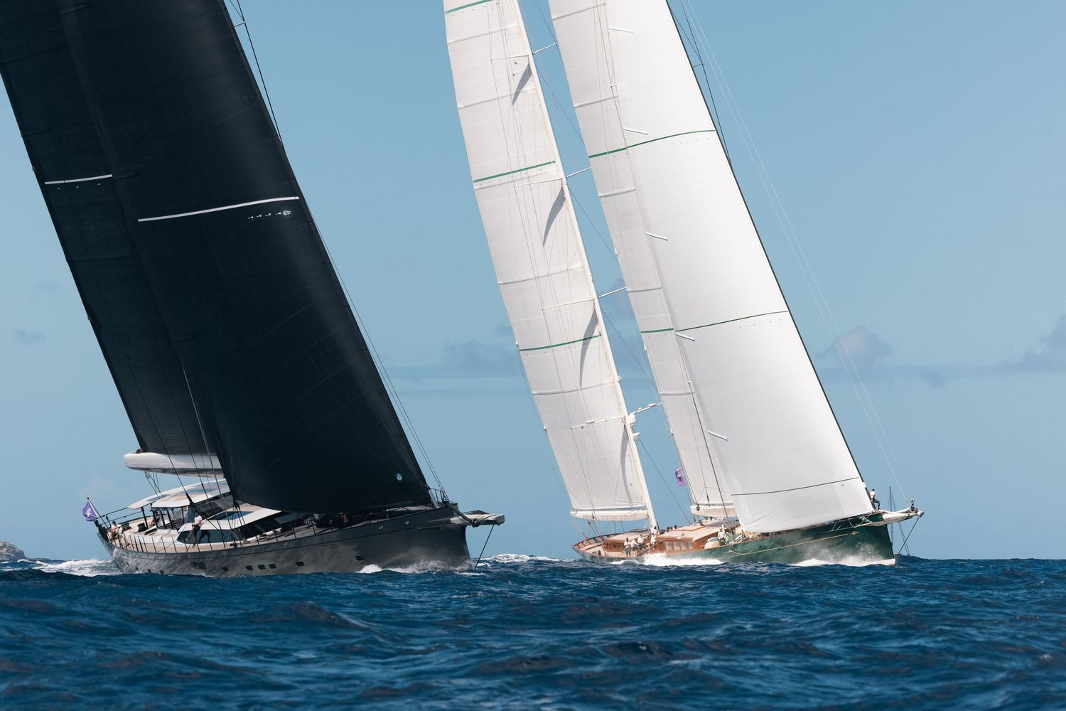 Multiple sailboats racing across blue ocean waters with white sails billowing in the wind.