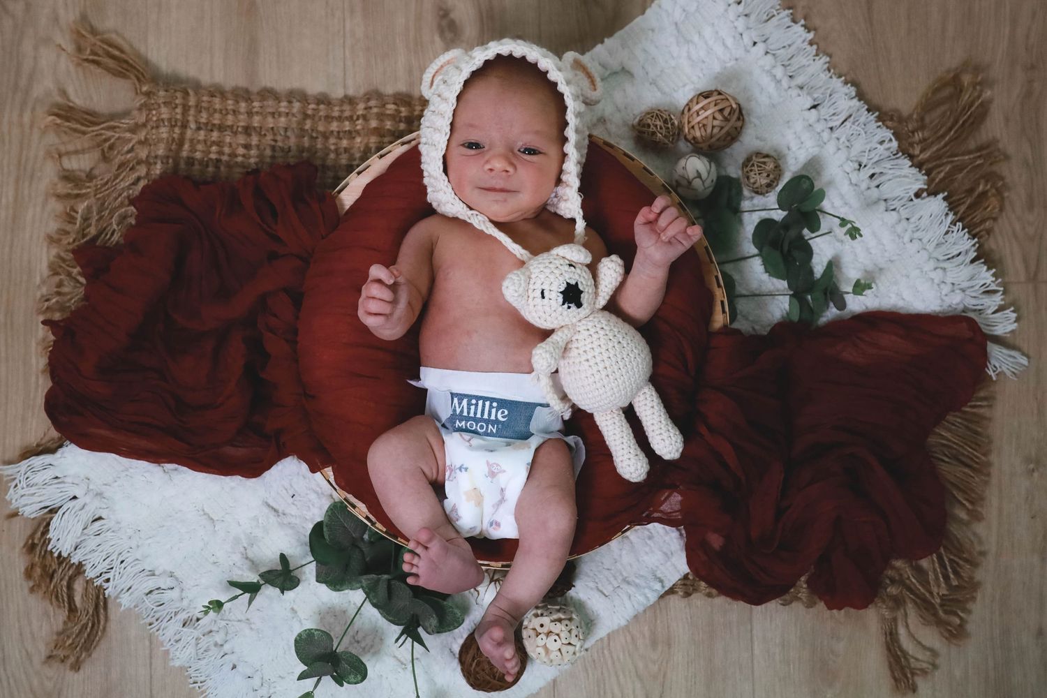 A baby lies on a white lace blanket with brown burlap backdrop and holiday decor surrounding them.