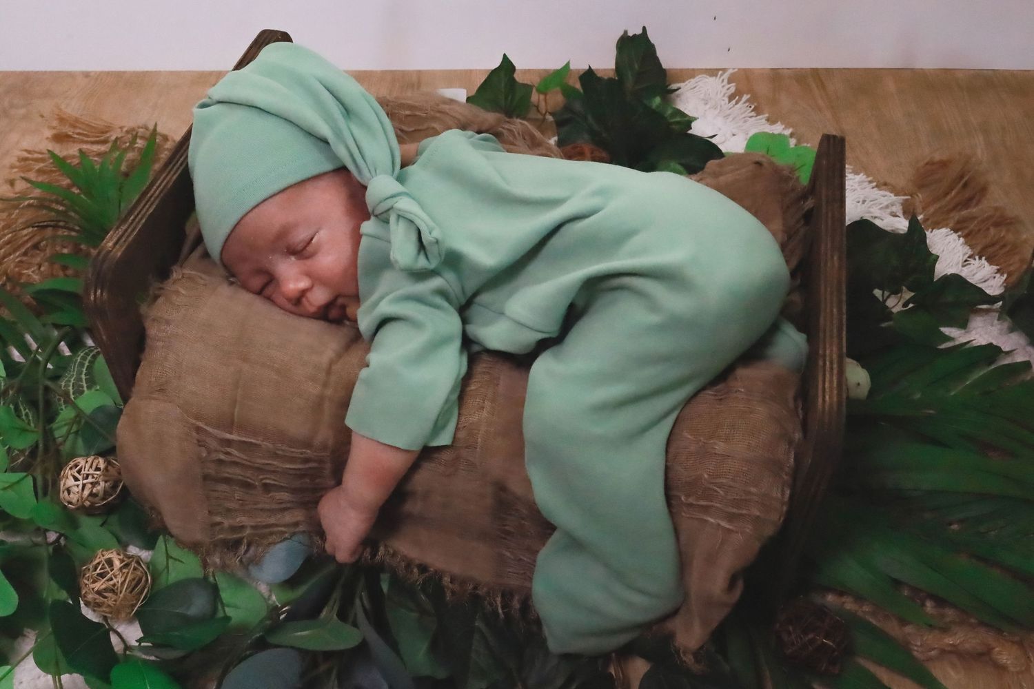 A small child in a mint green sweatshirt plays on a brown couch with green plants in the background.