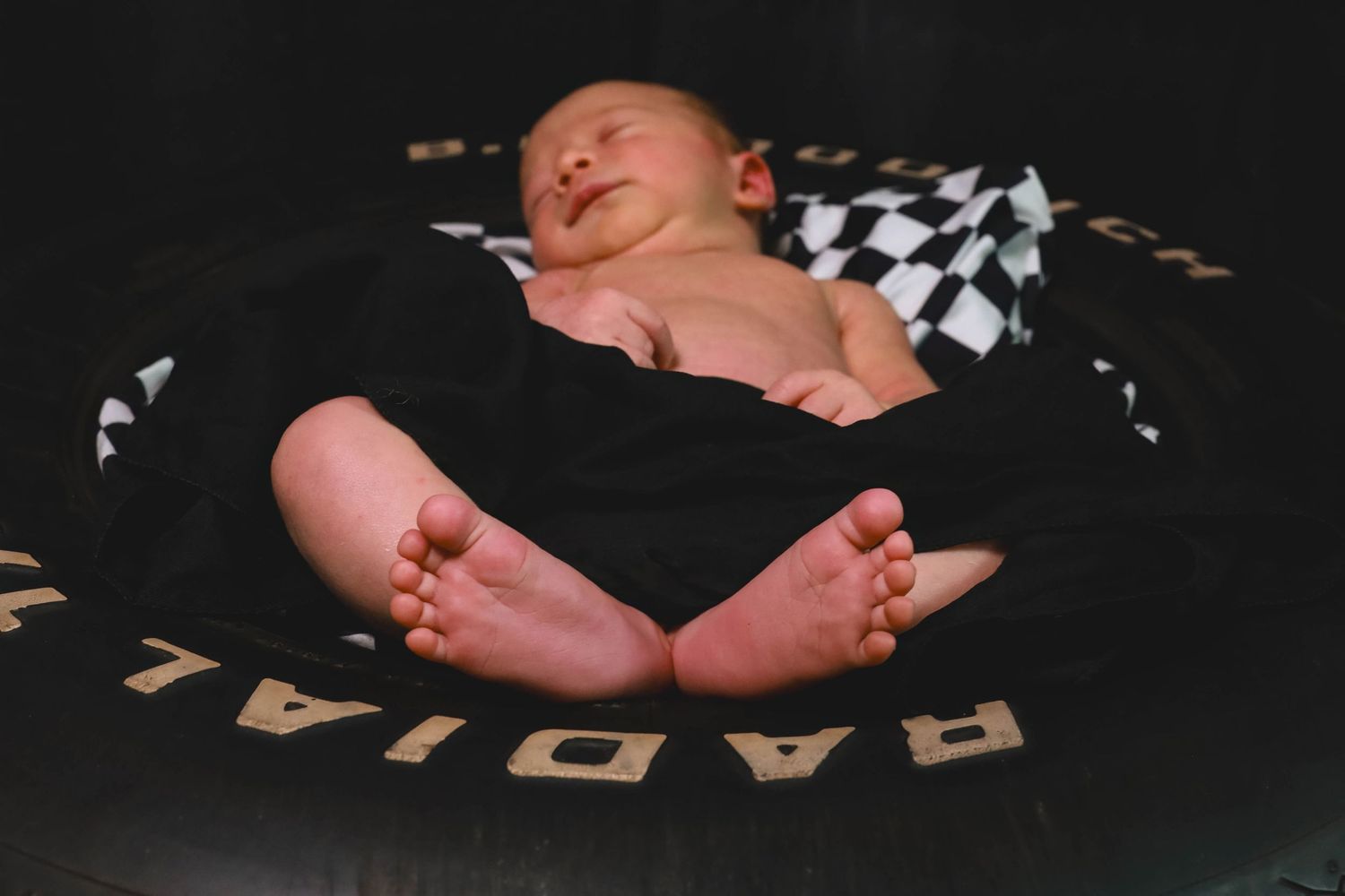 A newborn baby's tiny feet and hands are displayed against a dark background with scattered letter blocks.