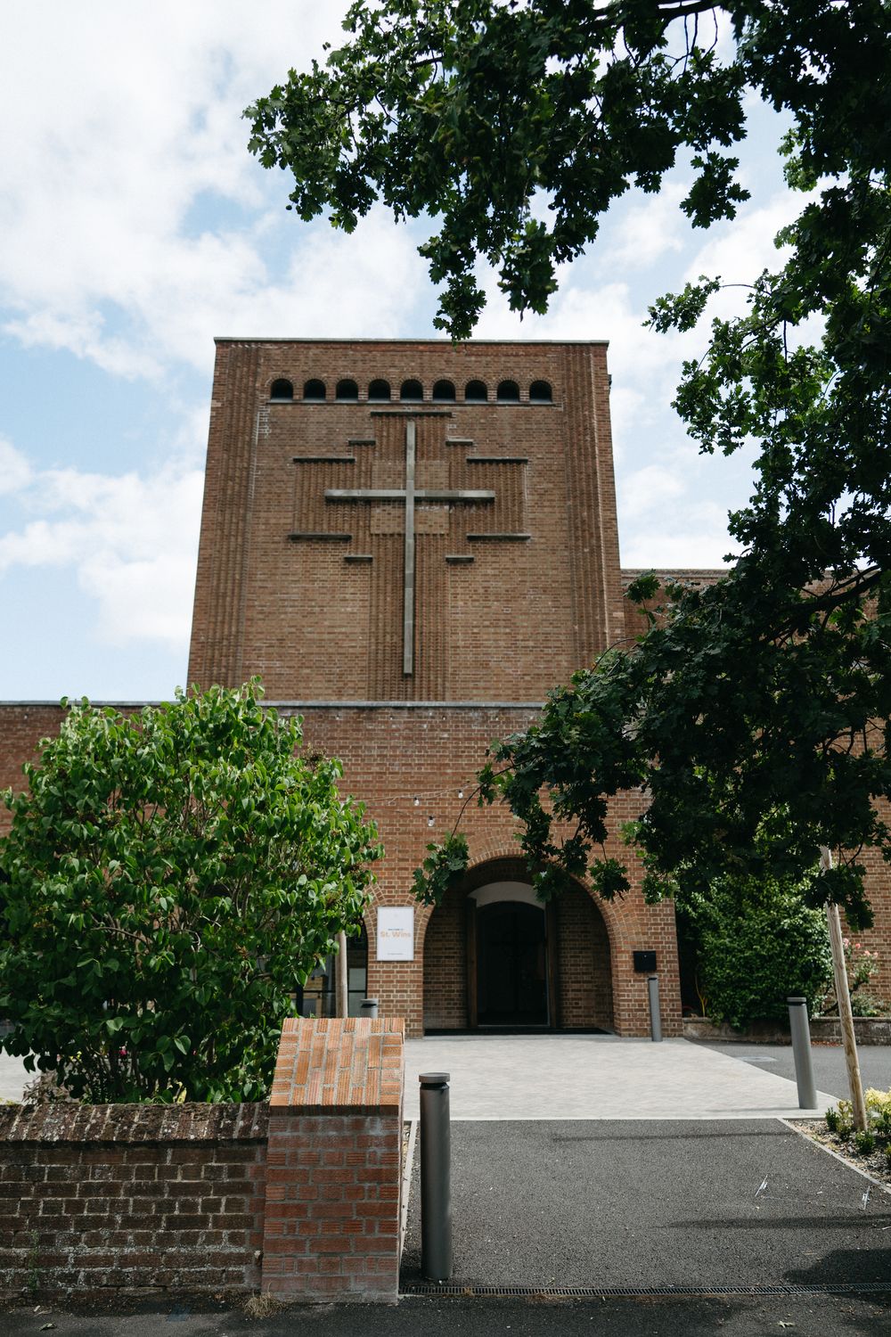 Four sequential views of a brick church entrance with arched windows and doorway framed by green trees and foliage.