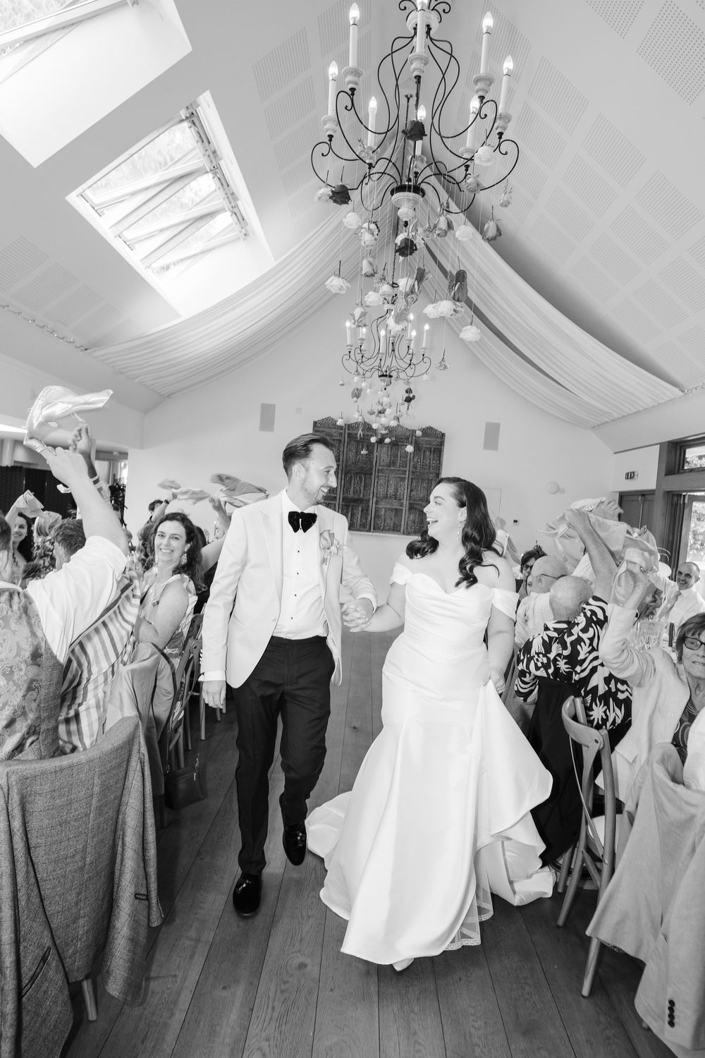 Wedding guests dance and celebrate in an elegant white room with chandeliers during a lively reception. Taken by editorial photographer.