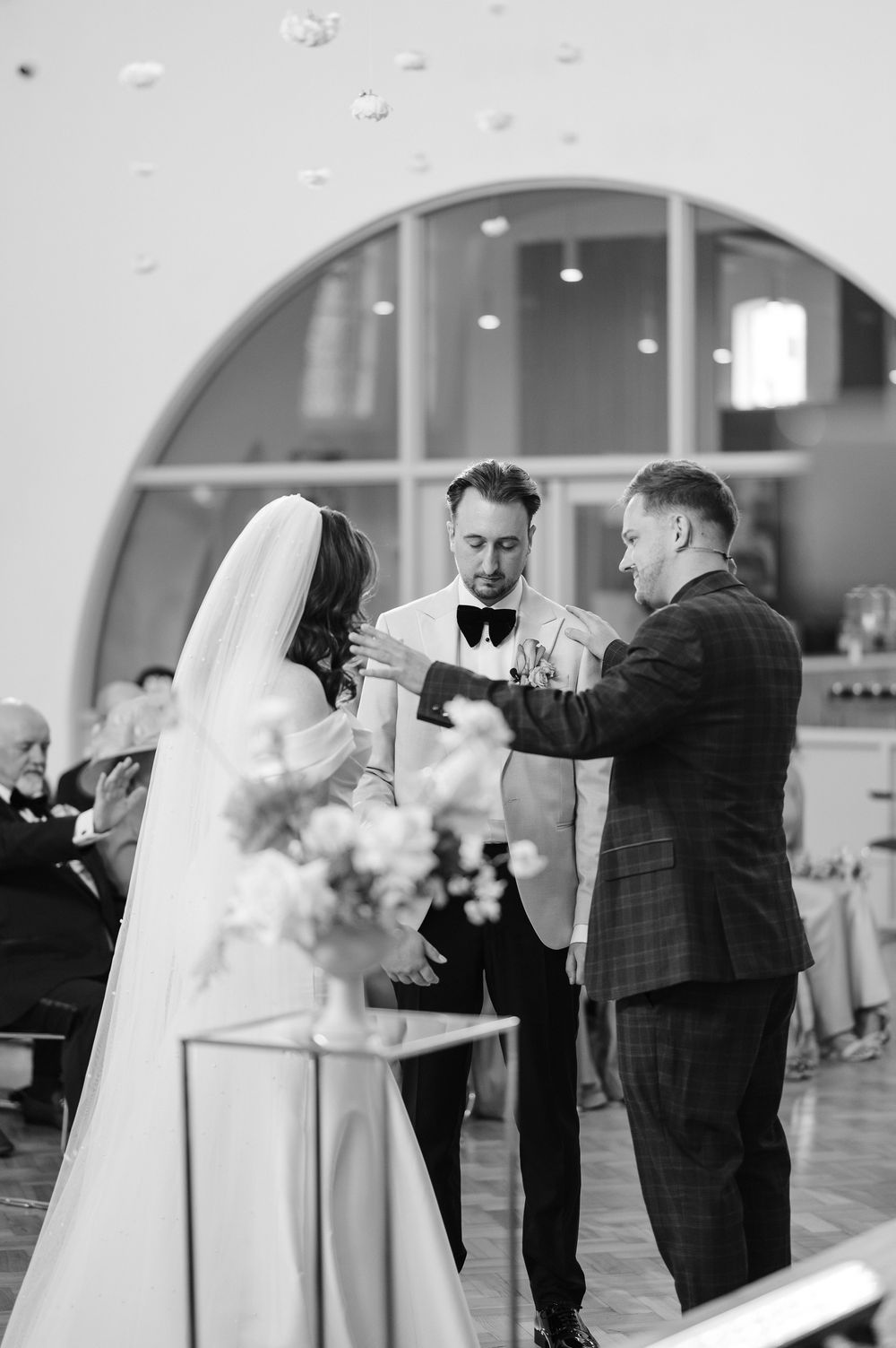 A series of black and white wedding ceremony photos showing intimate moments between a couple and officiant at an indoor venue.