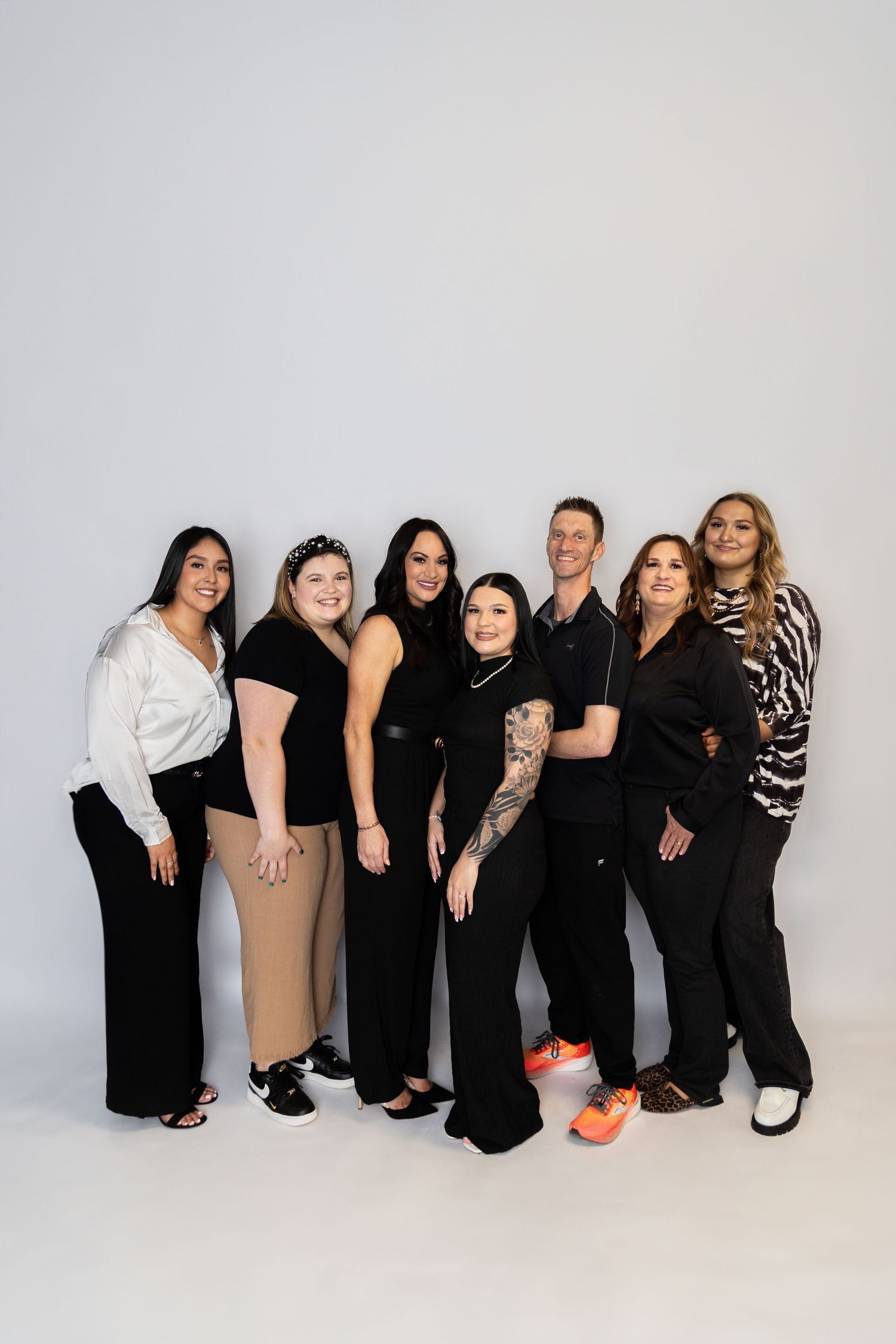 Group photo of people wearing black and neutral colored outfits sitting together against a white background.