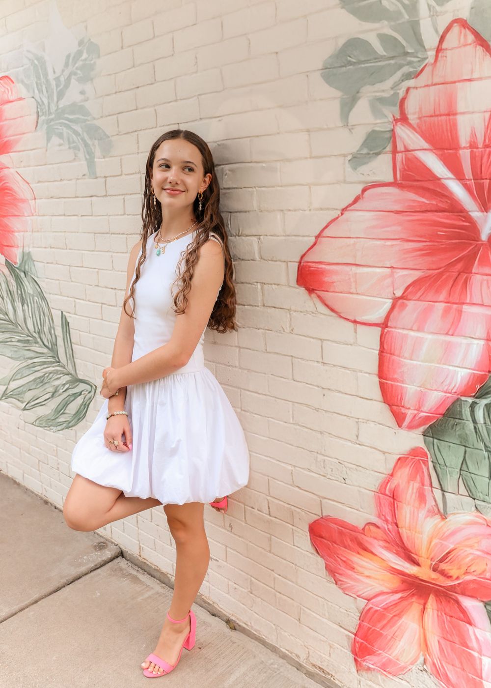 Teen girl in a white summer dress standing in front of a Hawaiian mural on a brick wall- natural outdoor portrait photography in Utah