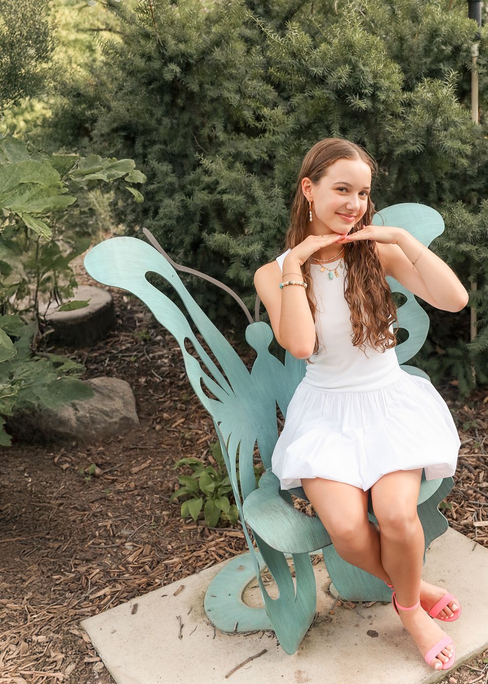 Teen girl in a white summer dress sitting on a teal butterfly chair, smiling with fun gesture - natural outdoor portrait photography in Utah