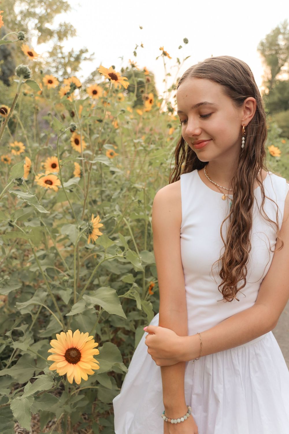 Teen girl in a white summer dress standing in a sunflower field, smiling with eyes closed - natural outdoor portrait photography in Utah