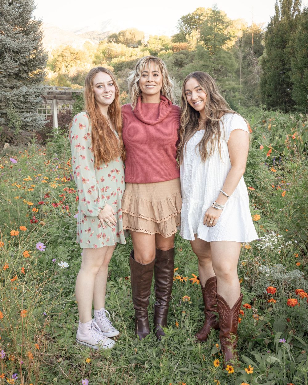 Three friends stand together in a wildflower field with orange poppies during golden hour.