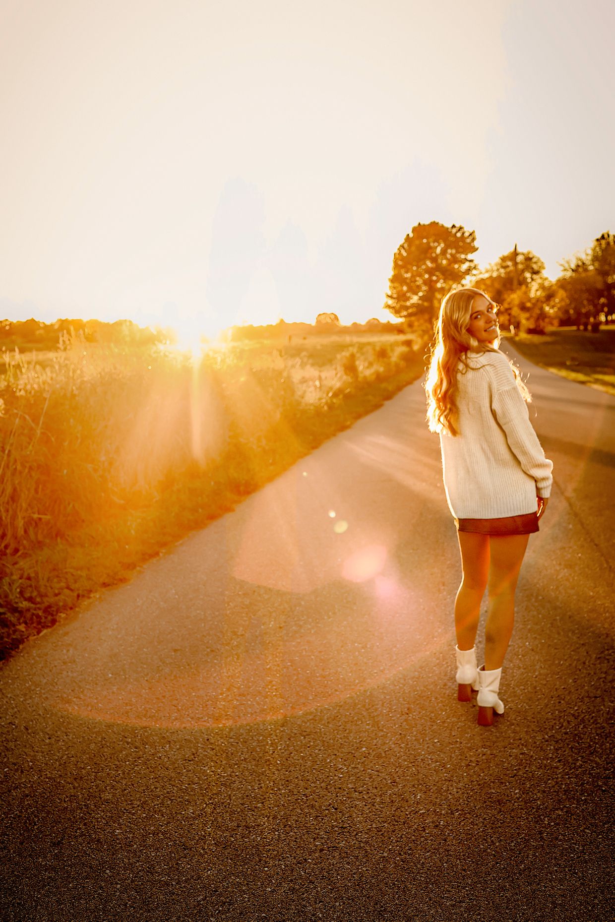 High school senior girl wearing white sweater walking on road during golden hour in Springfield MO