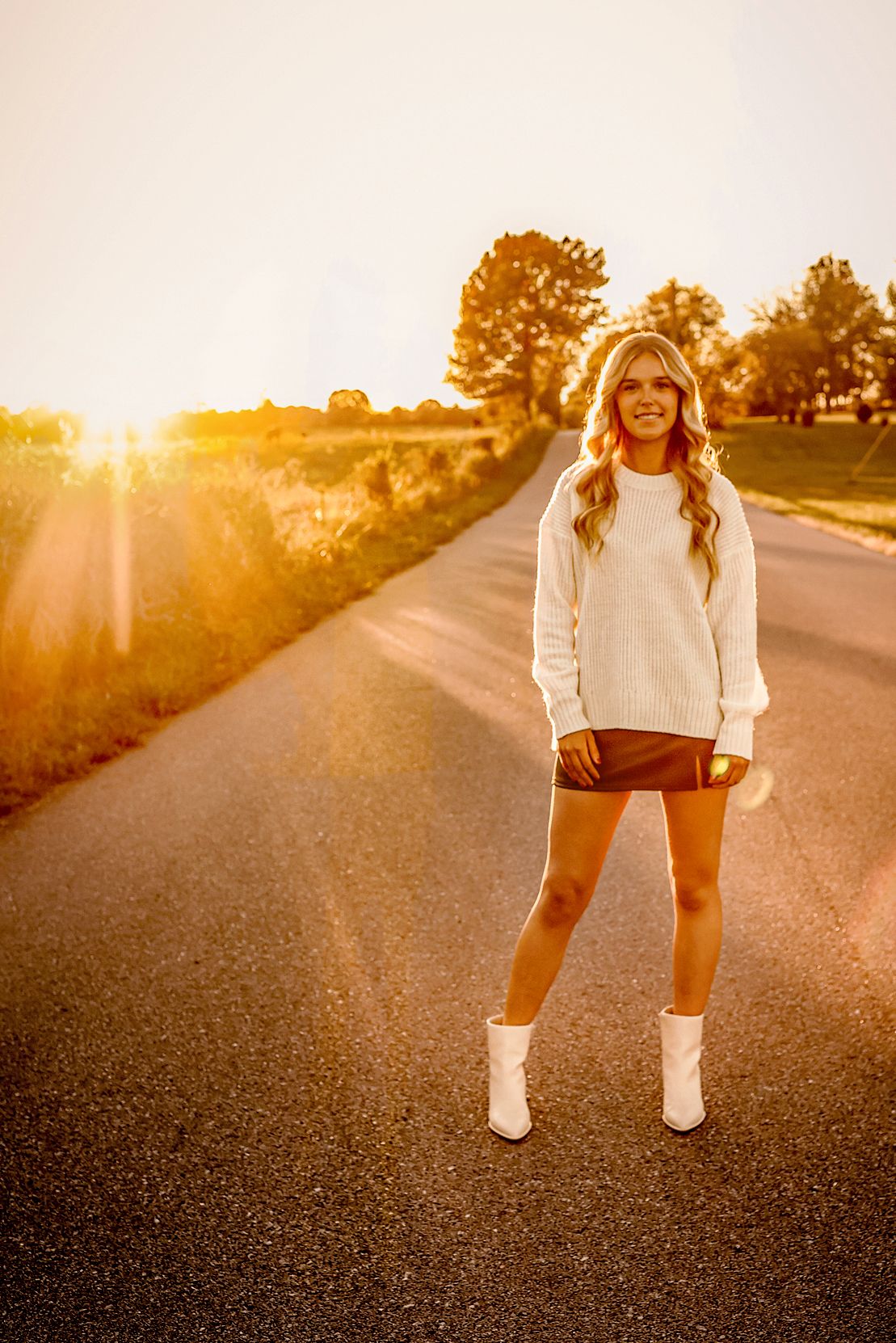 High school senior girl wearing white sweater walking on road during golden hour in Springfield MO
