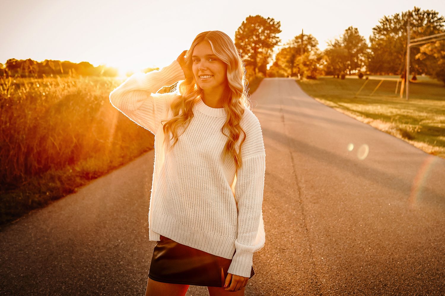 High school senior girl wearing white sweater walking on road during golden hour in Springfield MO