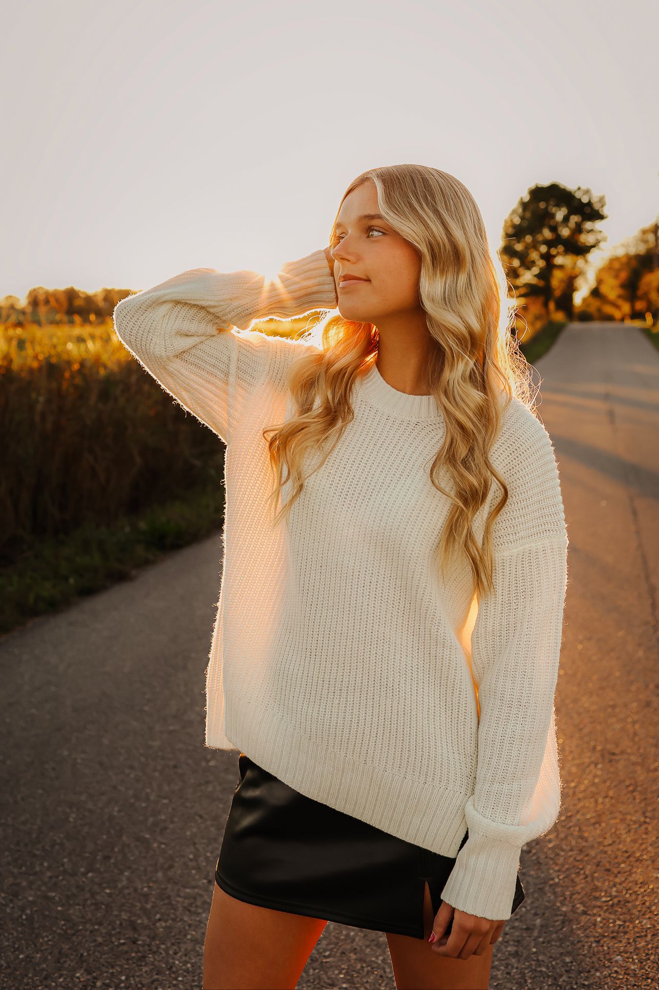 High school senior girl wearing white sweater walking on road during golden hour in Springfield MO