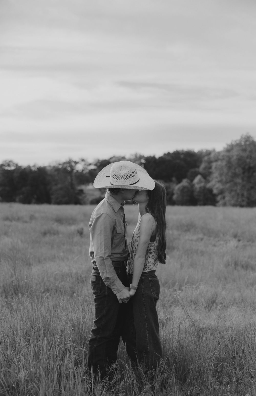 A romantic black and white photo series showing a couple holding hands and embracing in a rustic field.