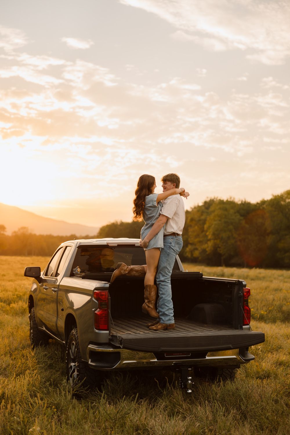 Couple embracing in the bed of a black pickup truck at sunset in a golden field.