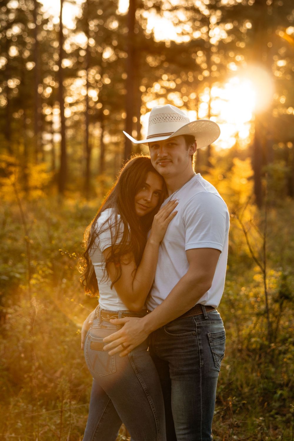 A couple embraces in a sun-drenched forest during golden hour, creating a romantic silhouette against the warm light.