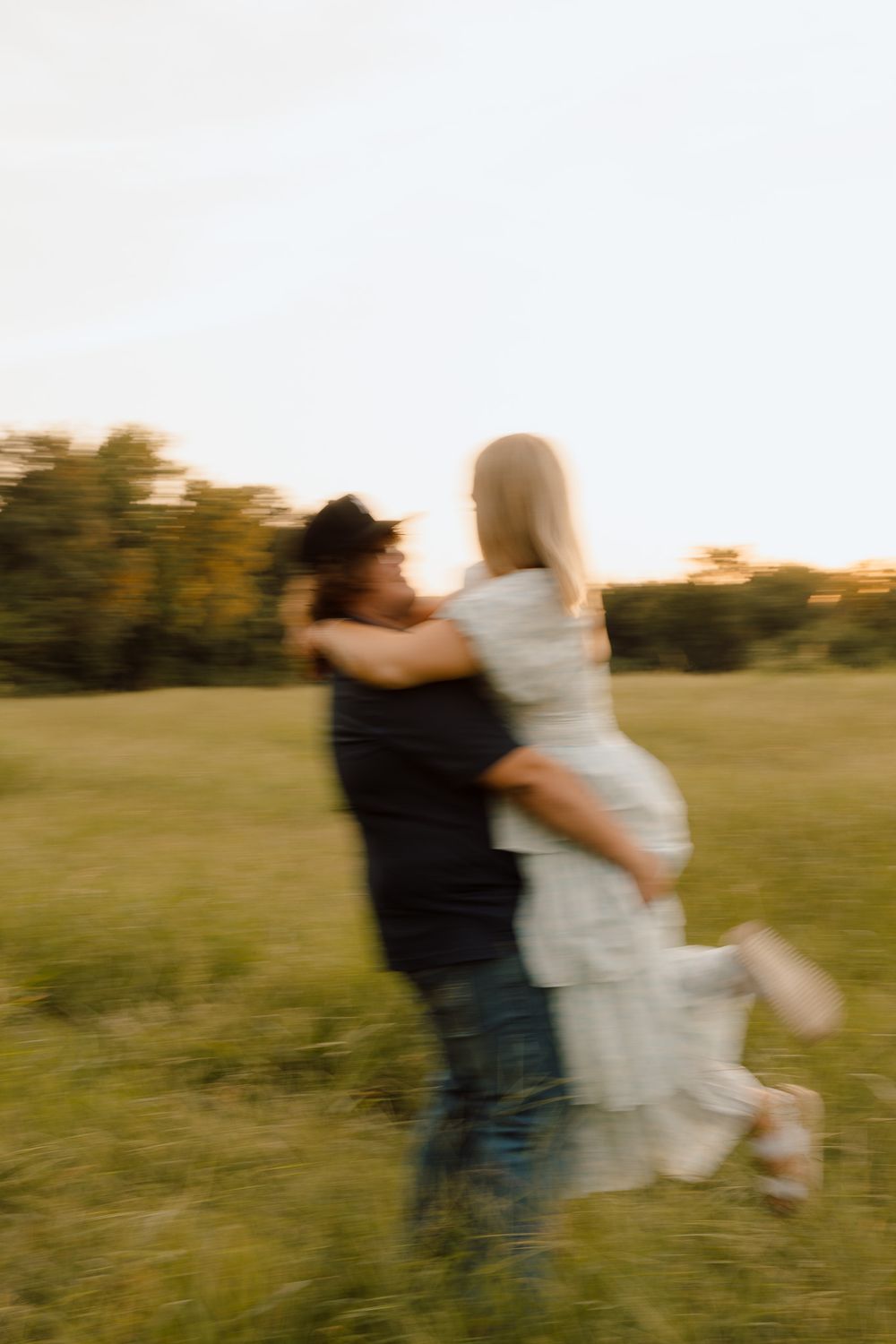 A blurred motion shot of a couple embracing and spinning in a grassy field at golden hour.