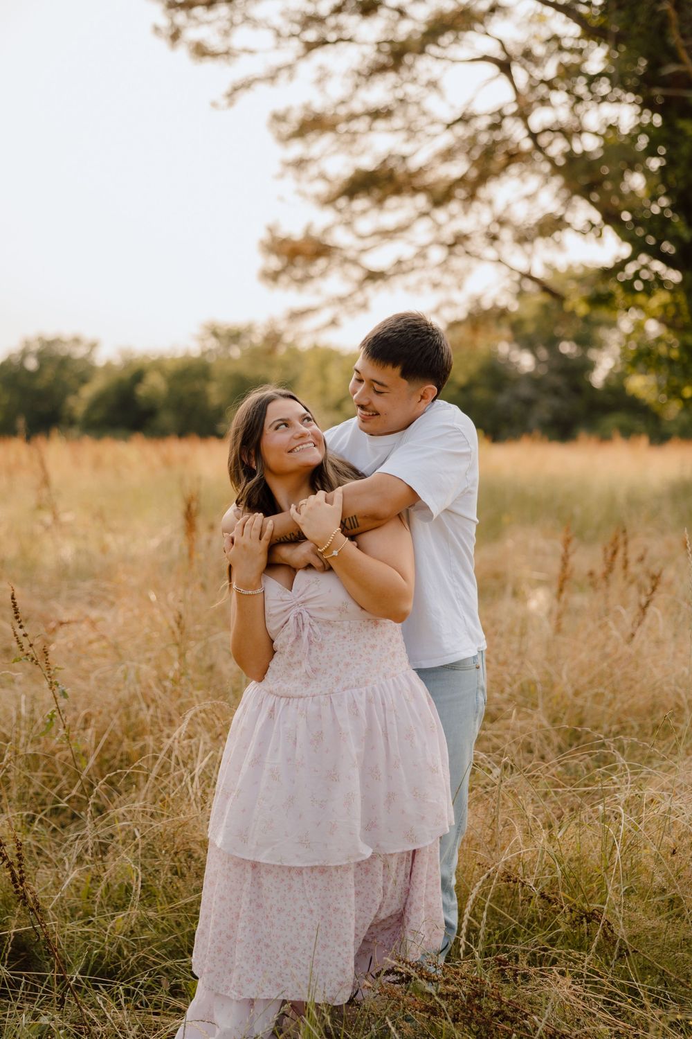 A couple shares a tender moment together in a sunlit golden field at sunset.