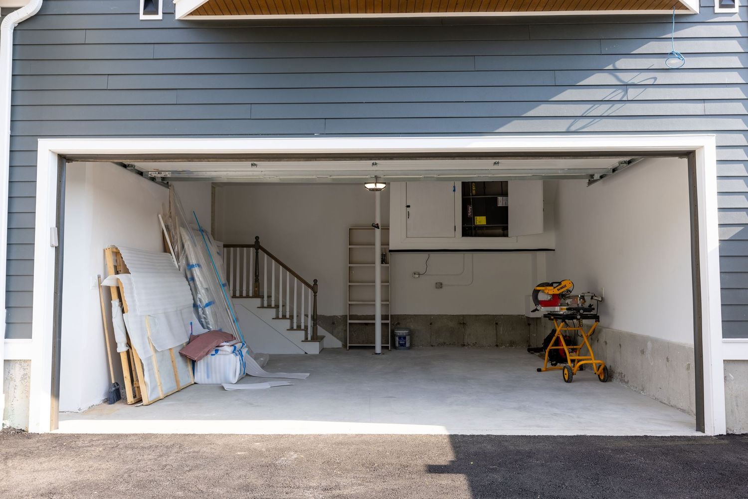 Empty two-car garage with concrete floors, white walls, and interior staircase access during renovation.