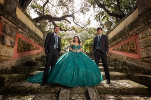 A group poses for photos in a garden setting wearing formal attire including an emerald green ball gown.